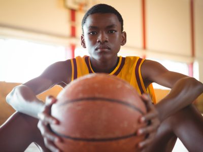 Close up portrait of teenage boy with ball sitting on floor in court